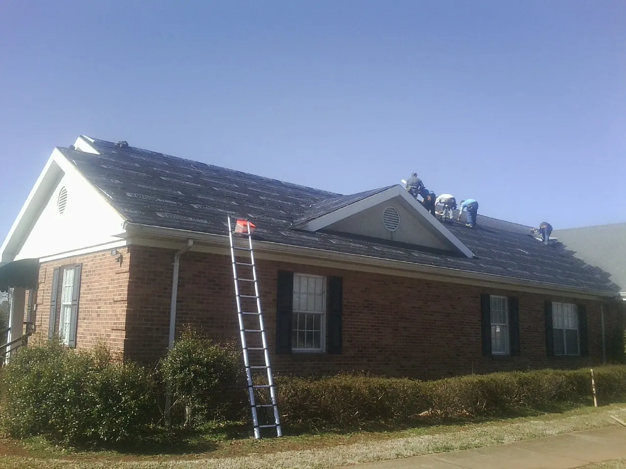 Crew tearing shingles off a brick ranch roof with a ladder set — Emergency Roof Repair work by our crew in Grover