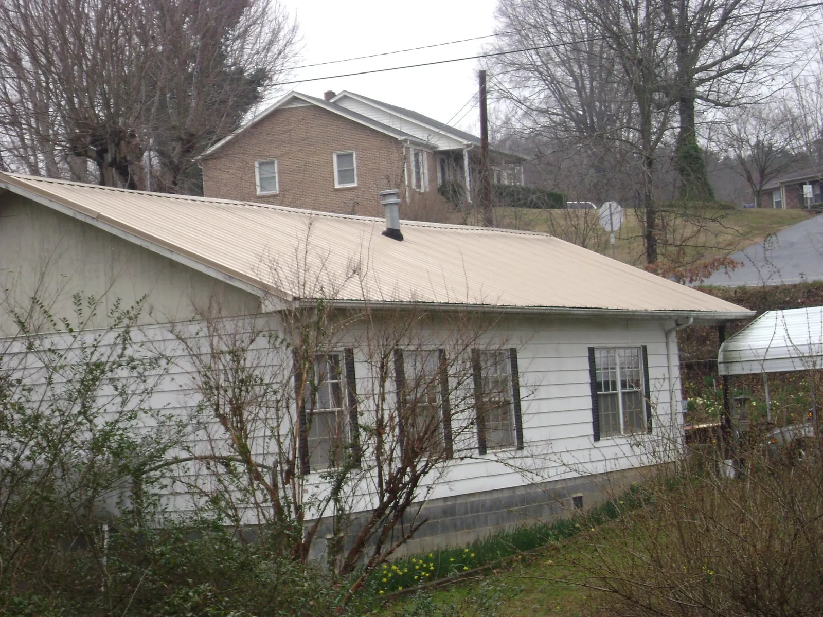 Tan metal roof on a white sided house set into a hillside — Commercial Roofing by Roofing Brothers in Grover